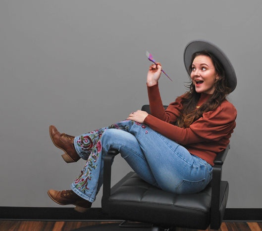 Kinsey Stokes seated in a salon chair holding a color brush